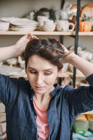 A beautiful young female potter collects her hair before starting work. Preparing for work of a...