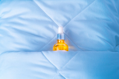 Glass bottle with serum, cosmetics on bed in bedroom. Cosmetic Essence for Night Skin Care, Minimal Conceptの写真素材