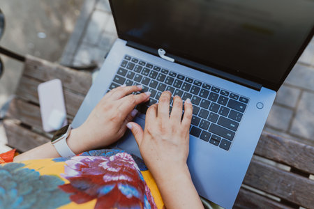 Female hands working on her laptop while sitting on a park. Working outdoors, a womans hands are typing text on a laptop keyboard, close-up, without a face.の写真素材