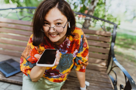 Smiling freelancer woman wearing colorful blouse, animatedly chatting on her smartphone outdoor....