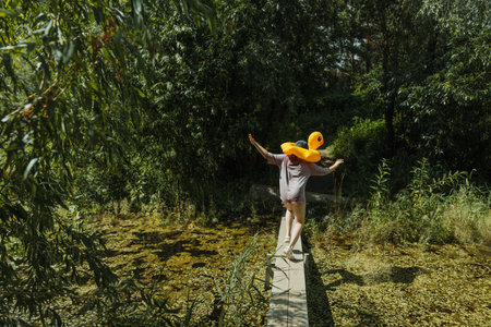 A child walking on a wooden bridge with a yellow duck float on her head. Concept of the end of...