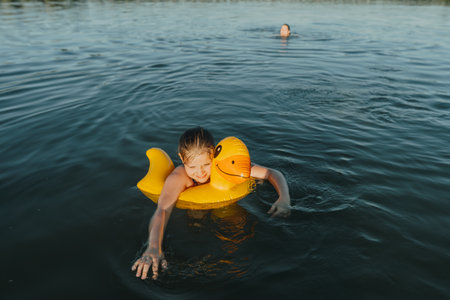 Smiling girl with an inflatable yellow duck swimming at the lake under the watchful eye of her...