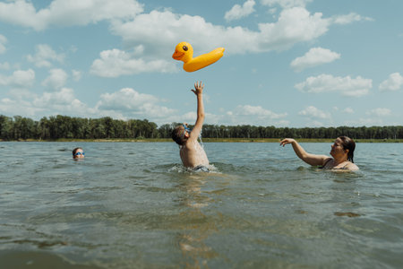 Joyful family playing in the lake with an inflatable duck float on a sunny summer day. The perfect way to spend time together during the holidaysの写真素材