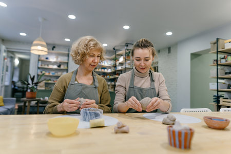 Teacher guides an elderly student, demonstrating sculpting techniques in a hands-on class. Senior...