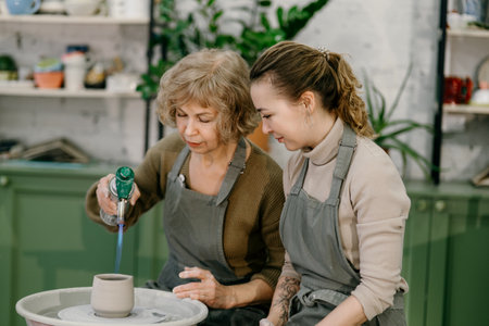 Hands-on learning, senior woman mastering pottery techniques using rotating wheel Mentor teaches...