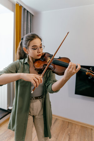 Female violin student plays notes at home preparing for upcoming performance. Focused young artist playing violin and studying music compositionの写真素材