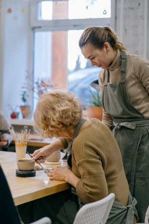 Happy retired student learns new skills, creating a handmade ceramic bowl. Female artist teaches an elderly woman how to shape clay at a hands-on master classの写真素材
