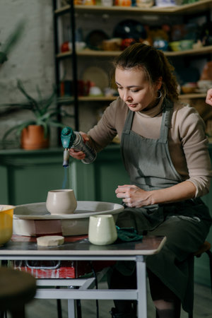 Young woman firing ceramic cup with gas torch at pottery workshop. Professional potter demonstrating firing technique with handheld torchの写真素材