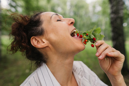 Woman in forest eating fresh wild berries on summer day natural food healthy eating theme. Happy woman eating strawberry in summer forest enjoying simple life mindfulness conceptの写真素材
