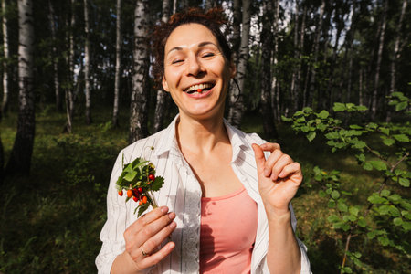 Woman eating wild strawberry sitting on grass in summer forest. Female enjoying nature, healthy...