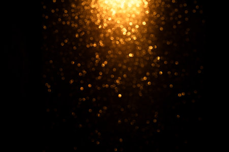 Glowing golden oval bokeh with shimmering light on dark background. Abstract festive glow with...