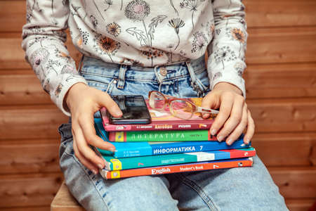 A teenage girl sits on a chair at home with textbooks, as she is self-isolating and studying at home in Russiaのeditorial素材