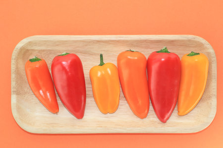 The view on the wooden tray with colorful paprika  on the orange backgroundの写真素材