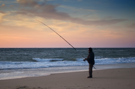 Man fishing in the beach shore at sunsetの写真素材