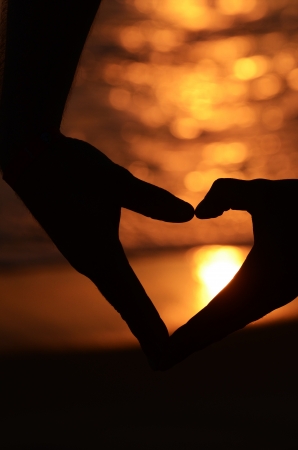 Hands forming a heart at the sunsetの写真素材