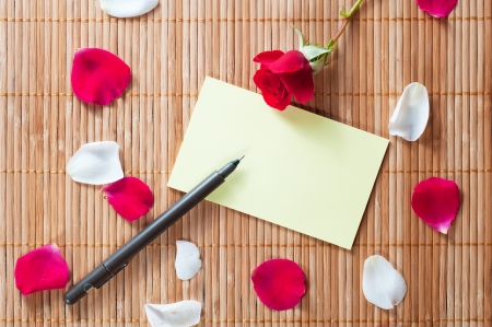 Pen and empty note on a wooden background with a rose and petalsの写真素材