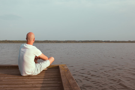 Man sitting in a wooden dock in a lakeの写真素材