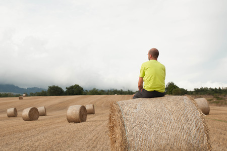 Young man in a field with straw bales. Resting on a baleの写真素材