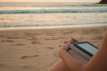 Woman reading in the beach with an ebook or tablet