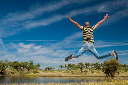 Man jumping in the pastures and pond in Extremadura, Spain. Many oak trees and blue skyの写真素材
