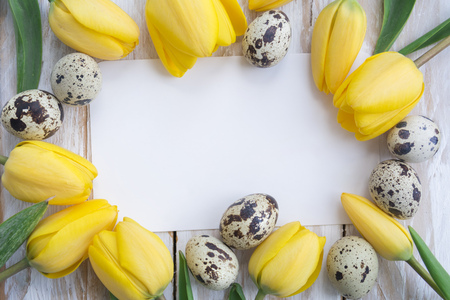 Quail eggs, yellow tulips and white card on wooden background. Easter concept Top view with copy spaceの写真素材