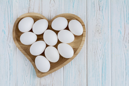 White eggs in wooden heart shaped plate on wooden white background, top view flatlayの写真素材