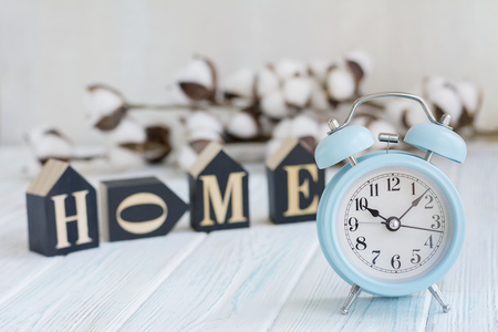 Beautiful white cotton flowers, cubes with letters and blue alarm clock on turquoise wooden background, home, morning conceptの写真素材