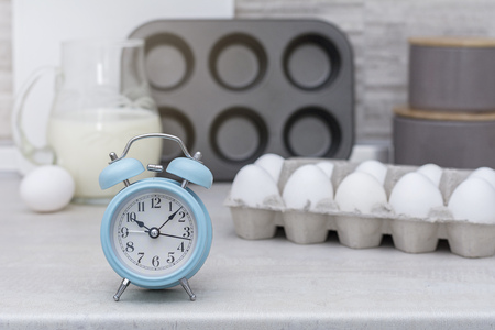 Light big kitchen. Tableware for cooking, cake mold and tray with eggs on the table. Blue alarm clock on table. Cooking preparations.の写真素材