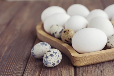White eggs and quail eggs in wooden heart shaped plate on wooden brown background, easter conceptの写真素材