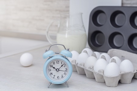 Light big kitchen. Tableware for cooking, cake mold, glass jar with milk, alarm clock and tray with eggs on the table.の写真素材