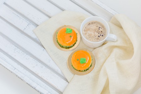 Bright orange mousse cakes and cup of coffee on white wooden trayの写真素材