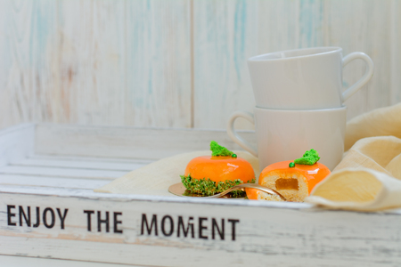 Bright orange mousse cakes and cup of coffee on white wooden tray, breackfast conceptの写真素材
