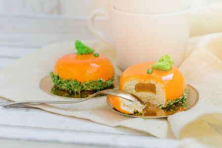 Bright orange mousse cakes and cup of coffee on white wooden tray, breackfast conceptの写真素材