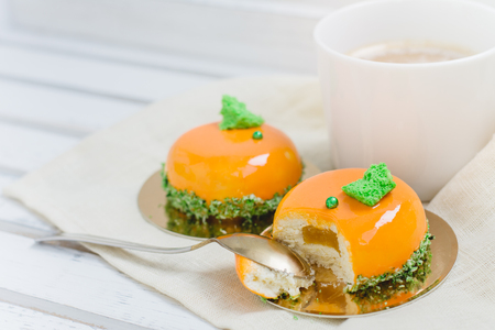 Tasty orange mousse cakes and cup of coffee on white wooden trayの写真素材