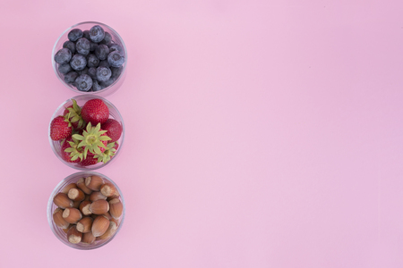Srawberry, blueberry and hazelnuts in glass cups on pink backgroundの写真素材