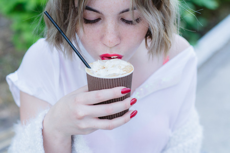 Girl with red lips takes a sip of cappuccino from paper cupの写真素材