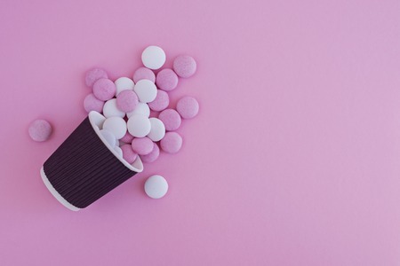 Pink and white round candies poured out of the cup on pink backgroundの写真素材