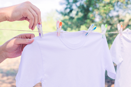 Hands are putting white laundry on a rope with plastic colorful clothespins to dry, outside, croppedの写真素材