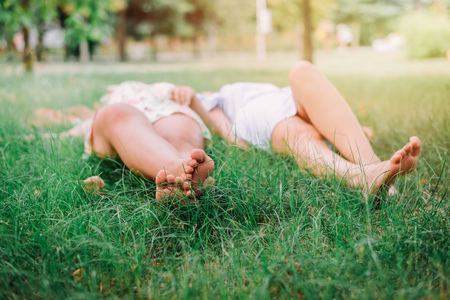 Bare feet of two young girls laying on green grass. Fiendship and freedom concept.の写真素材