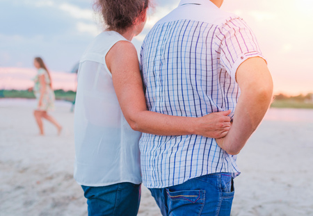 Cute mid-aged couple in love is holding their hands and walking together on the beach, love concept,...