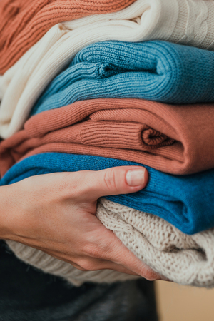 Stack of warm orange and blue pastel sweaters, holding in hands. Copy space.