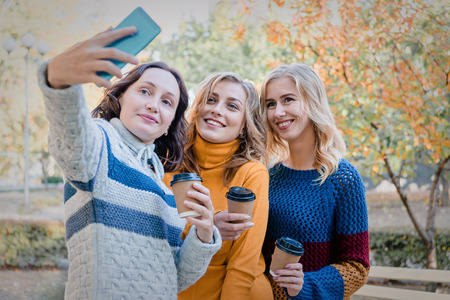 Cheerful attractive three young women best friends having fun together outside and making selfie.の写真素材