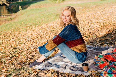 Attractive young woman with curly hair is sitting on warm blanket outside.