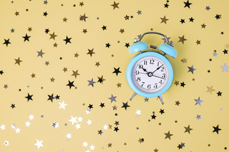 Blue alarm clock on yellow background with glitter star confetti.