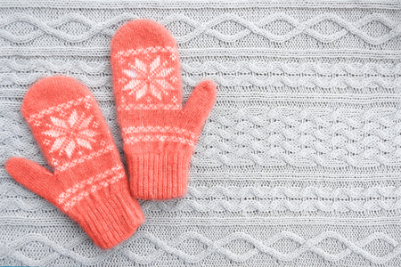 Warm woolen mittens on knitted background. Living coral creative and moody color of the picture....