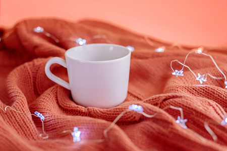 Tea cup on warm knitted coral blanket and star lights. Cozy and moody concept. Mockup.の写真素材