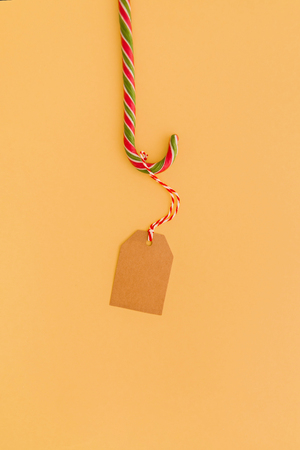 Christmas craft paper tag hanging on candy cane on yellow background. Minimal styled banner with copy space.の写真素材