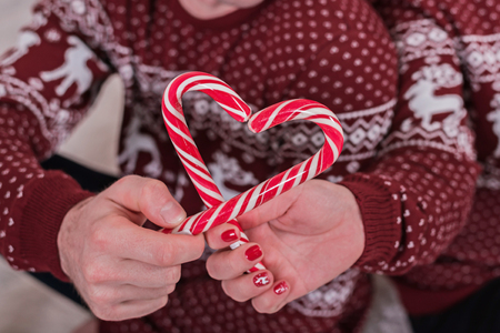 Heart of candy canes in hands of romantic couple in christmas sweaters. Cropped. Christmas mood.の写真素材