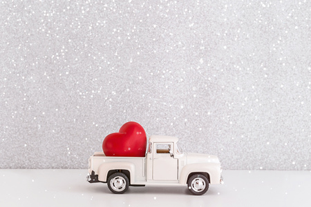 White retro toy car delivering heart for Valentine's day in toy snowy forest. Symbol of love.の写真素材