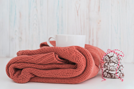Cup of coffee with milk and chocolate cookies on warm knitted coral blanket. Cozy and moody concept.の写真素材